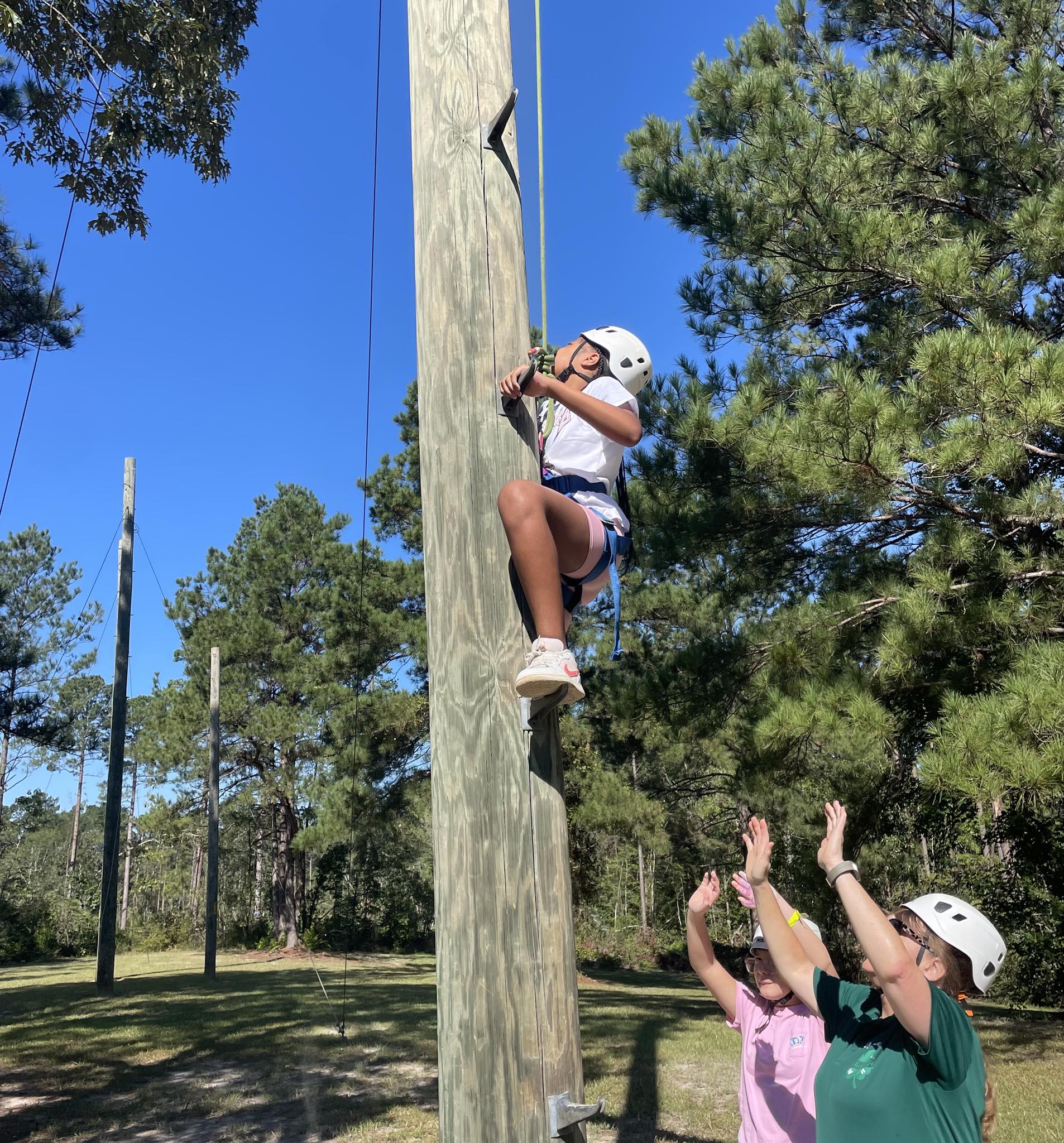 A kid wearing a helmet and climbing a telephone pole.